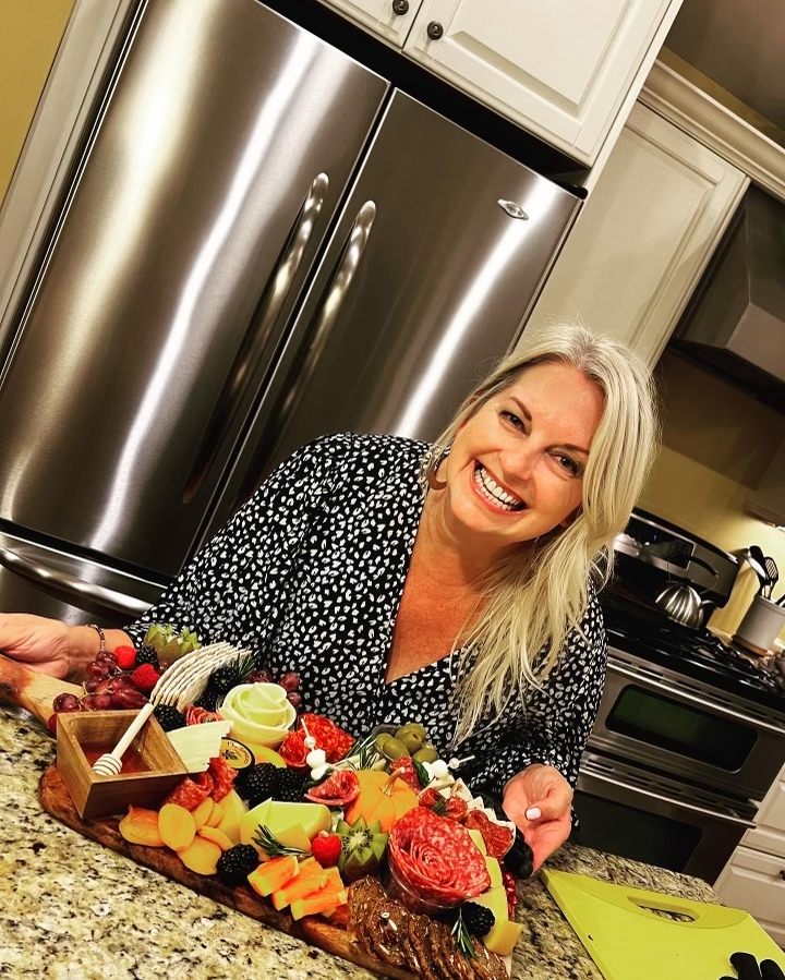 A photo picturing Michelle kneeling behind a counter, where there is one of her beautiful charcuterie boards in the foreground