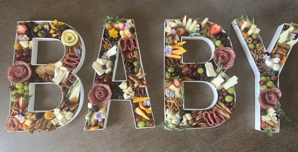 Four charcuterie boards, arranged into letters spelling the word "Baby."